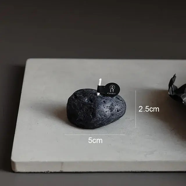 Bougie parfumée géométrique météorite noire sur surface blanche avec dimensions indiquées de 5 cm de largeur et 2,5 cm de hauteur.